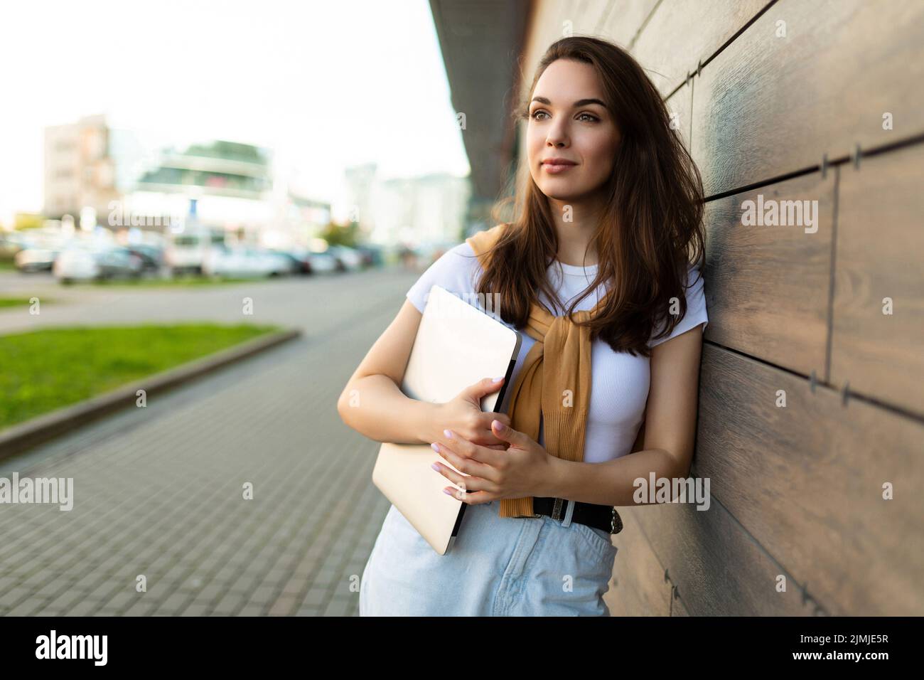 Photo of pretty attractive beautiful wonderful positive charming young brunette young woman holding grey computer laptop wearing Stock Photo
