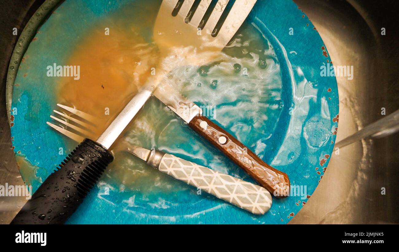 A dirty fork and spoon on a blue plate in a dishwasher Stock Photo