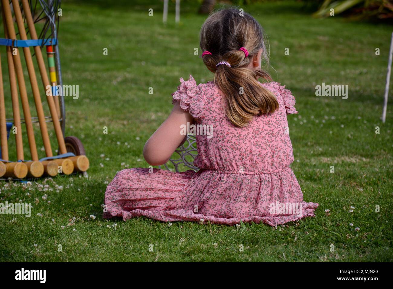 A little girl wearing a pink dress sitting on the ground Stock Photo ...