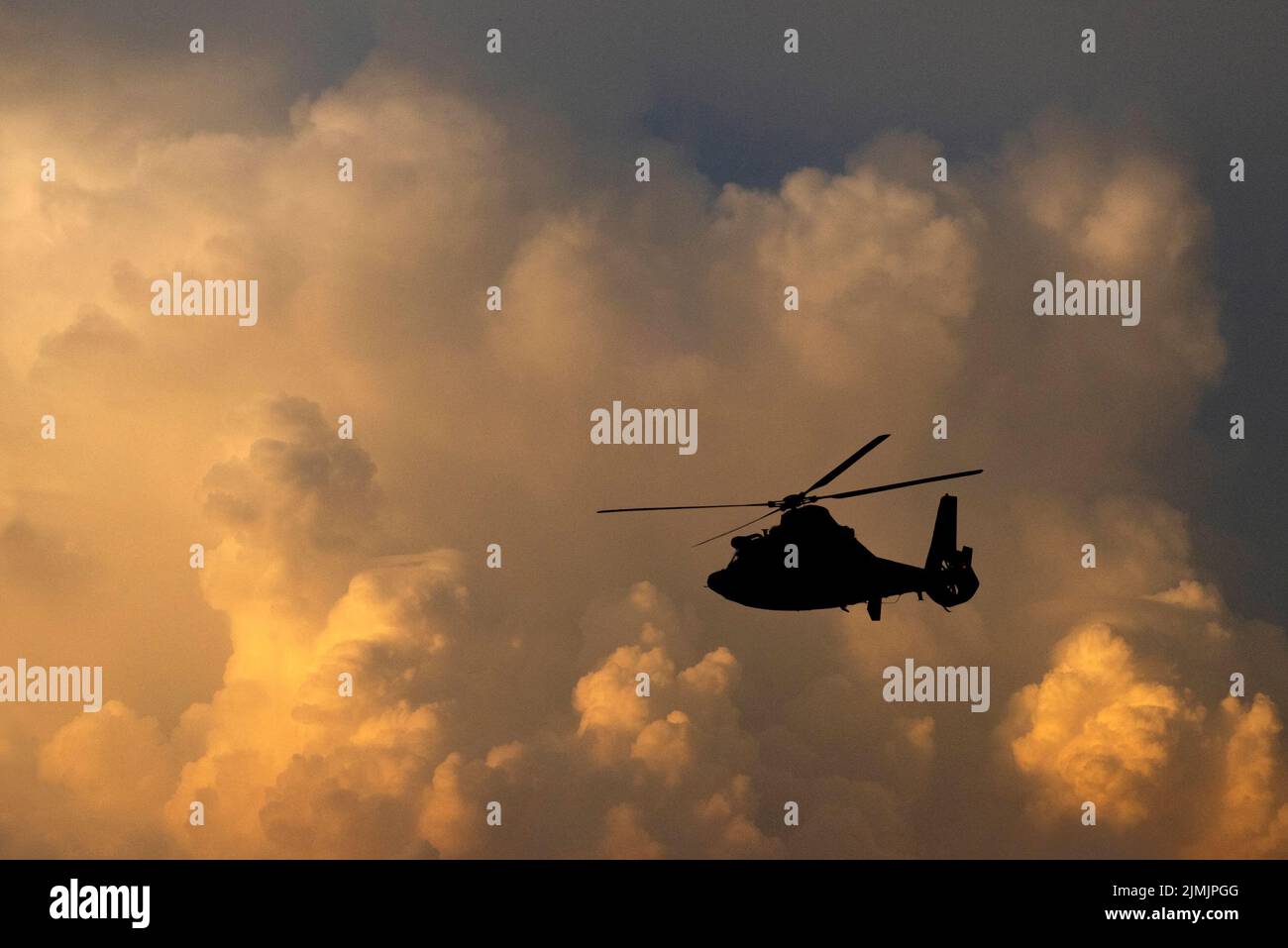 A U.S. Coast Guard helicopter in silhouette against a cloudy sky in a composite image. Stock Photo
