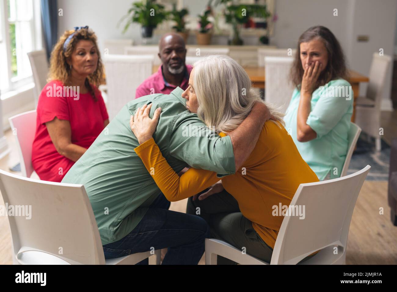 Caucasian senior man and woman embracing during group therapy session. unaltered, support, alternative therapy, community outreach, mental wellbeing a Stock Photo