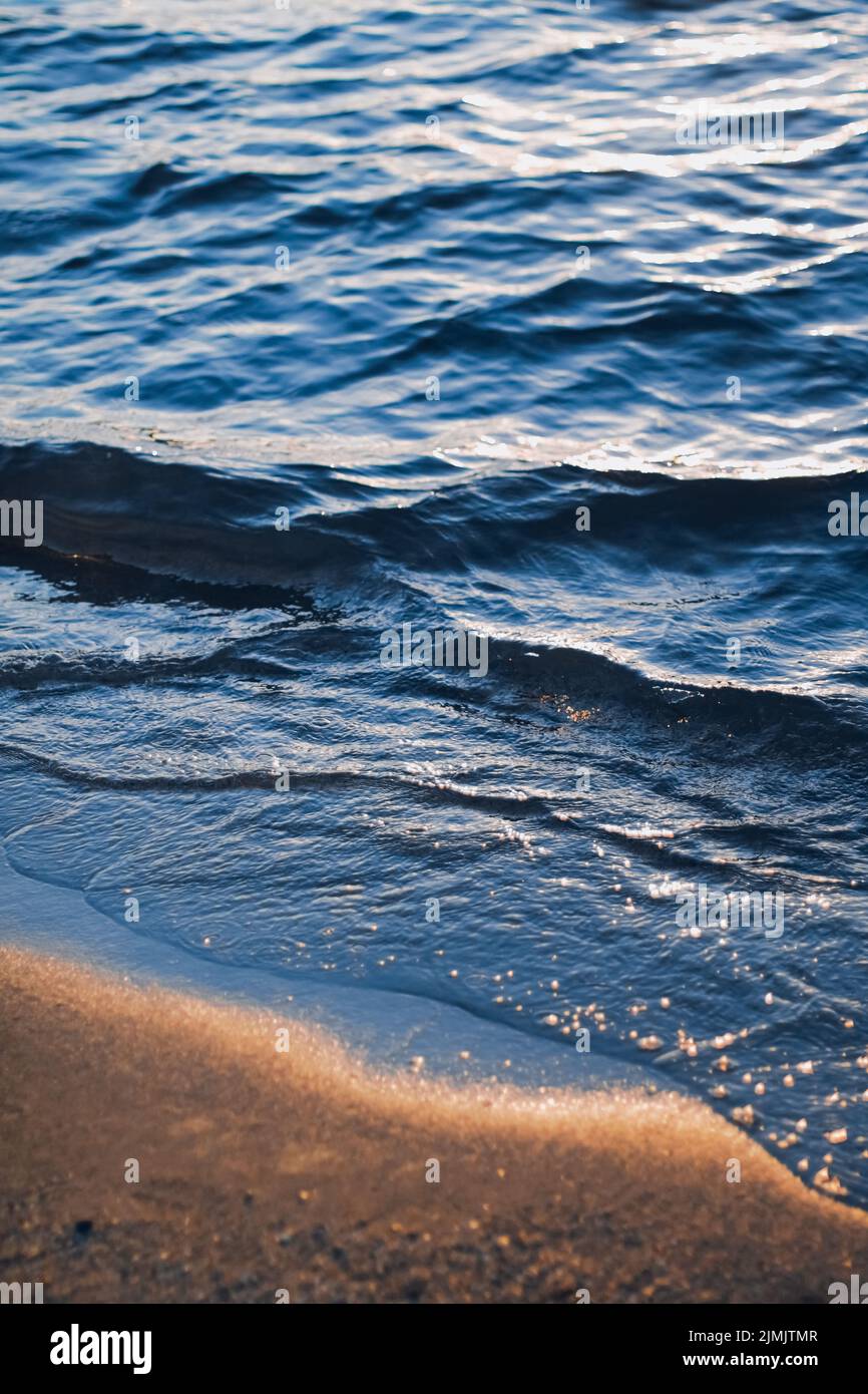 Blue sea waves and golden sand in sunshine glow at sunset, sandy beach
