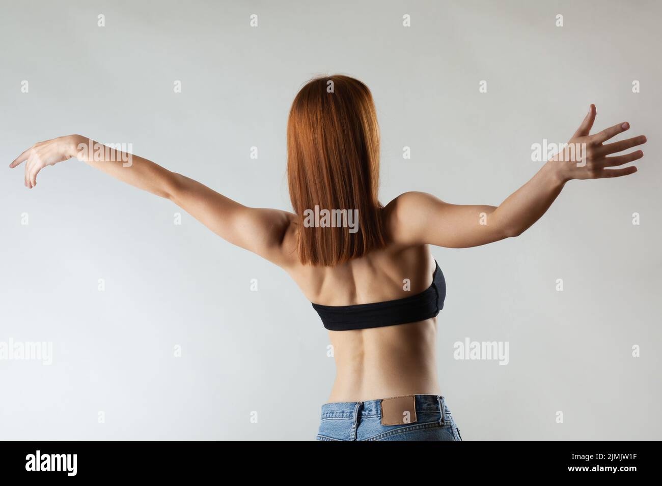 Beautiful girl with burnt orange hair stretching and making ballet pose. Studio portrait on gray background. Stock Photo