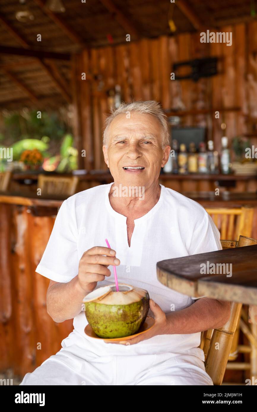 Happy senior man is drinking a coconut water in the beach bar Stock