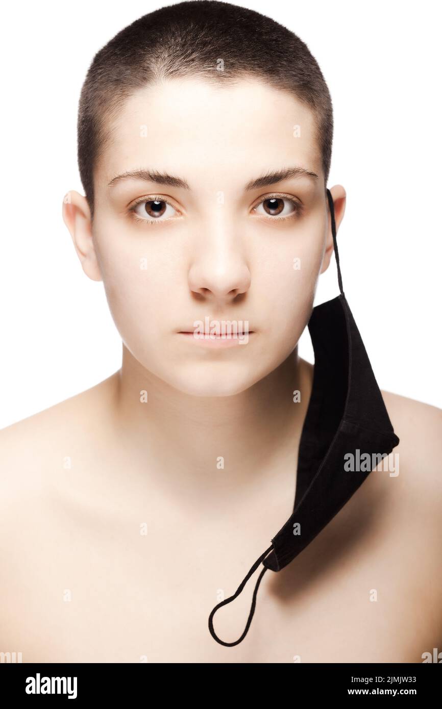 Cute girl with very short hair wearing black protective face mask hanging on her ear. Studio portrait isolated on white background Stock Photo