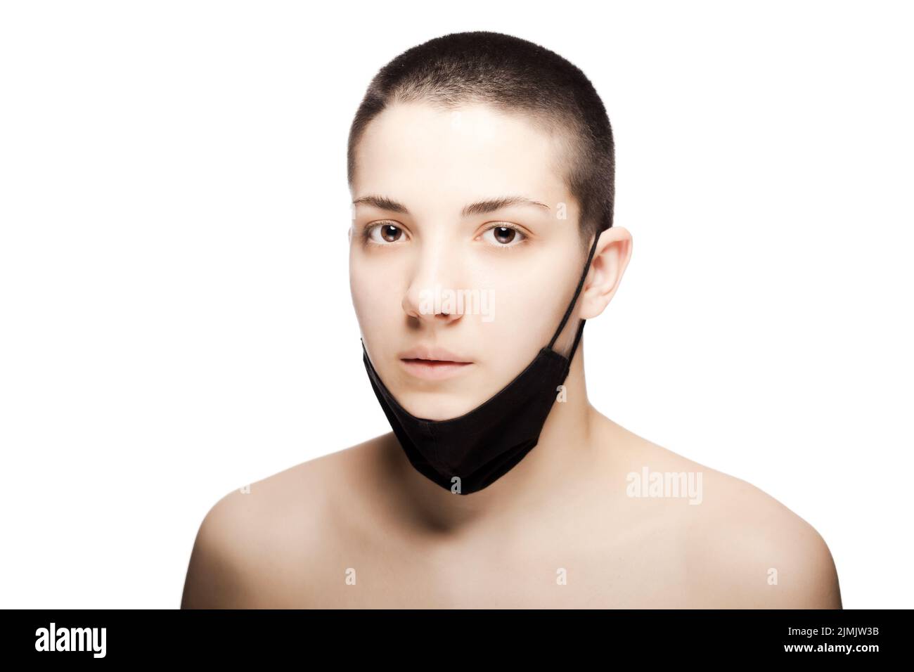 Cute girl with very short hair wearing black protective face mask under her chin. Studio portrait isolated on white background Stock Photo