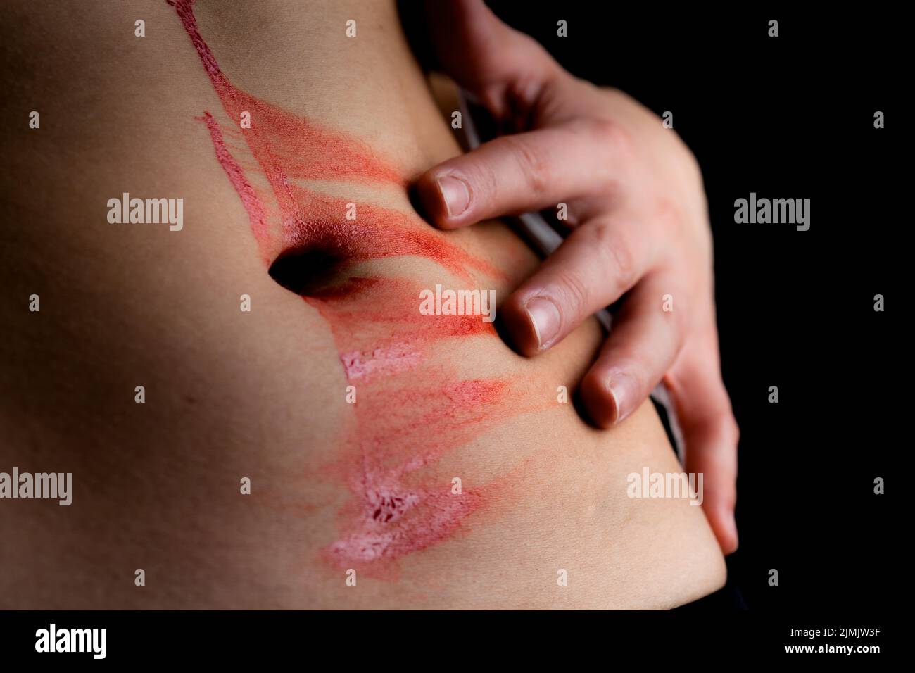 Drop of blood on female body. Hand smearing red liquid flowing on and off belly button. Stock Photo