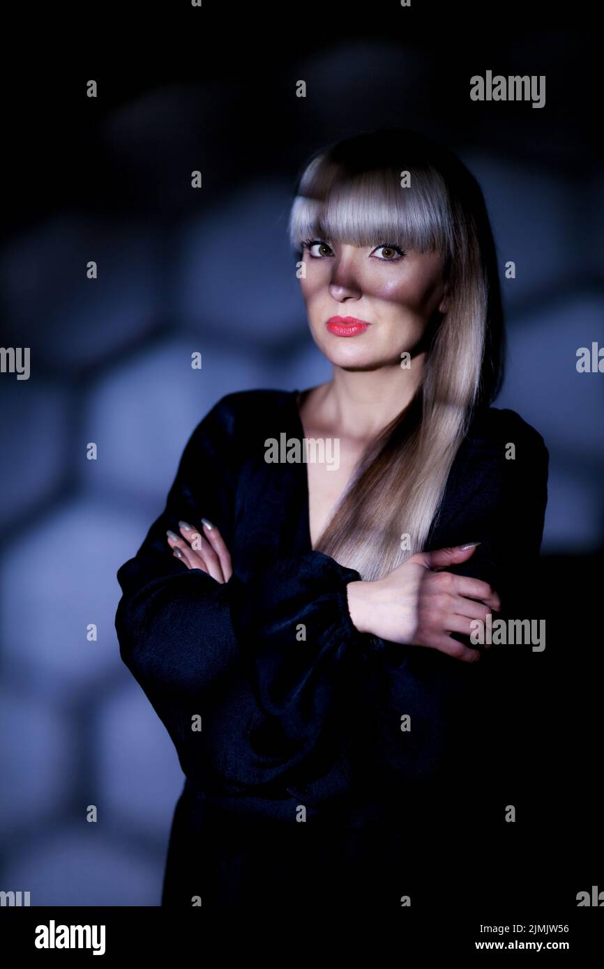 Beautiful girl with blond bangs fringe wearing black fashionable fancy dress posing under shadows Stock Photo