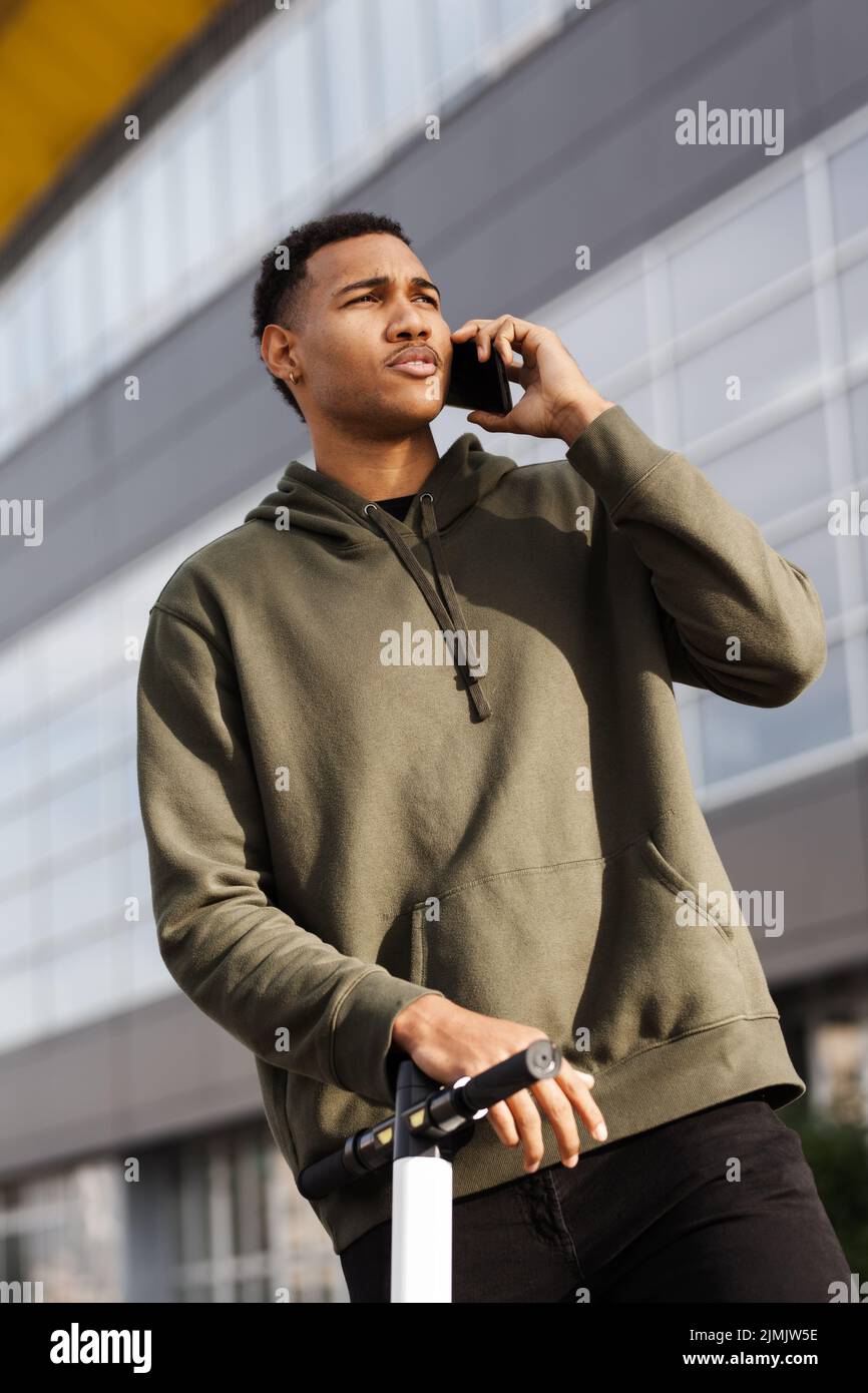 young african american man in casual outfit standing with electric scooter and talking on phone Stock Photo