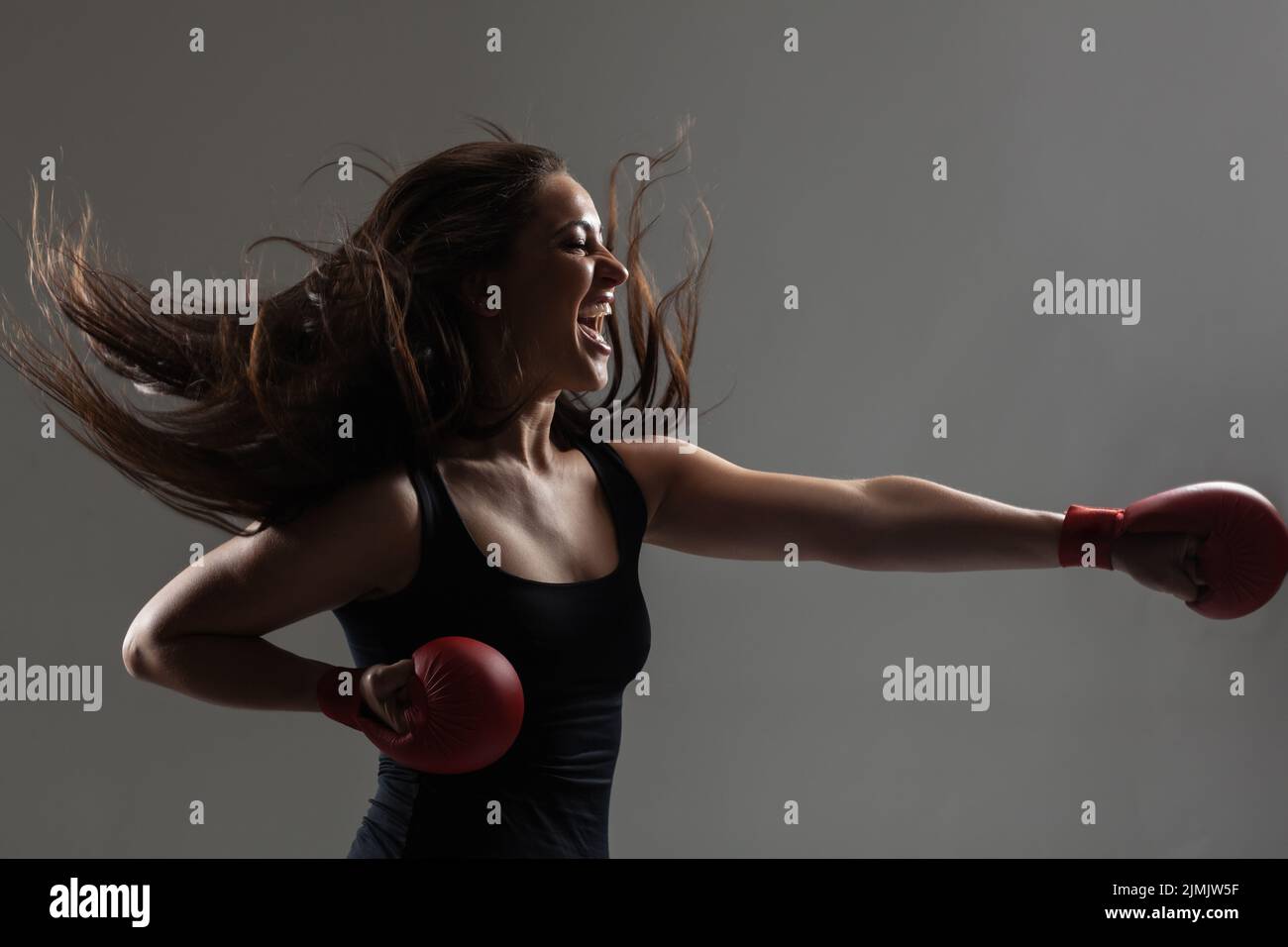 beautiful girl exercising karate punch and screaming against gray background Stock Photo