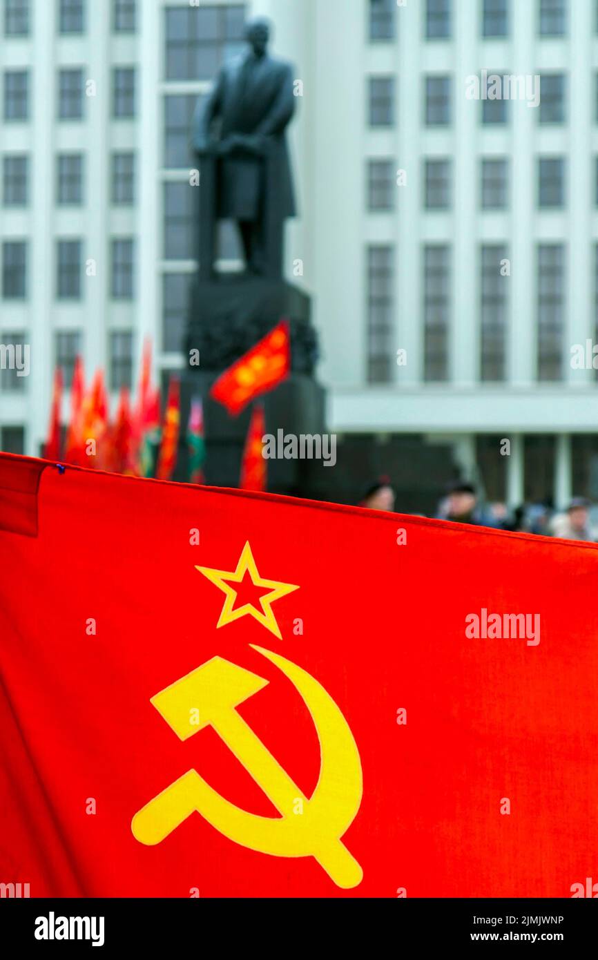 Soviet scarlet flag with hammer and sickle and star. In the background is a blurred figure of Lenin Stock Photo