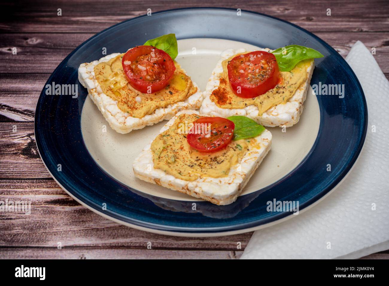 Three Rice crackers with chickpea hummus, cherry tomato and fresh basil
