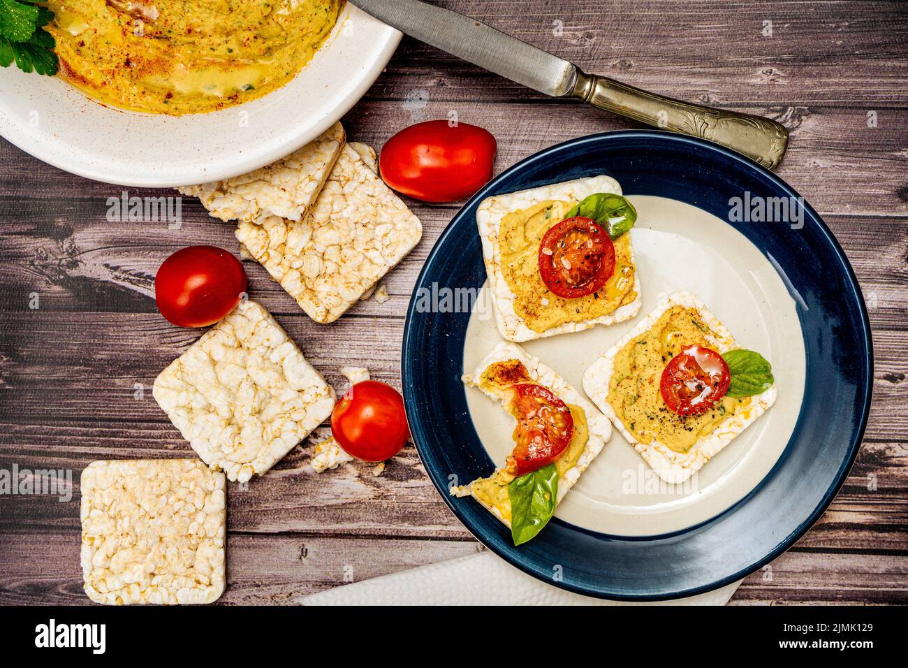 Square rice crackers with hummus and cherry tomatoes on a plate
