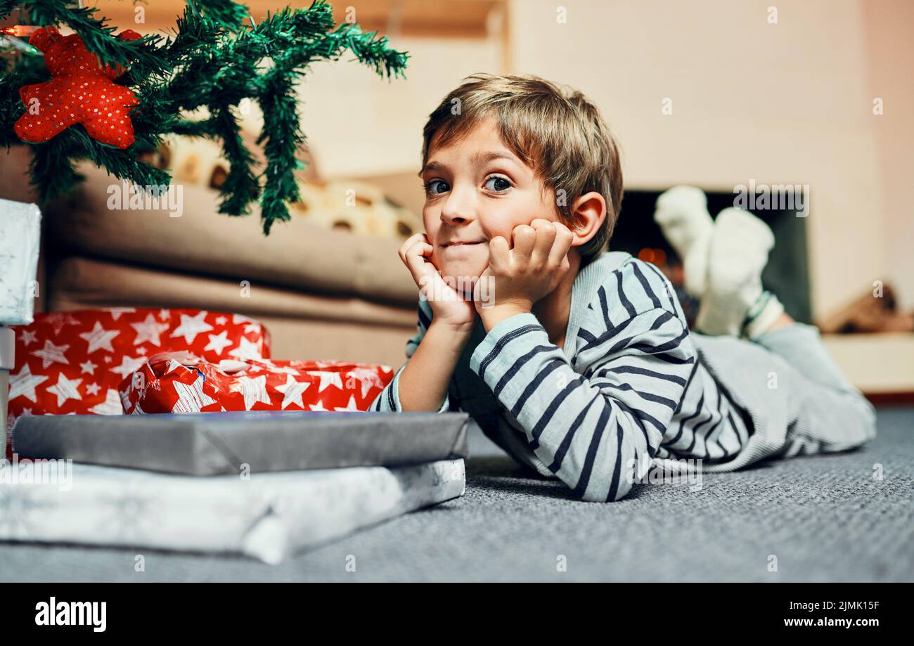 Patience...soon the presents will be opened. an adorable little boy lying down next to the Christmas tree at home. Stock Photo