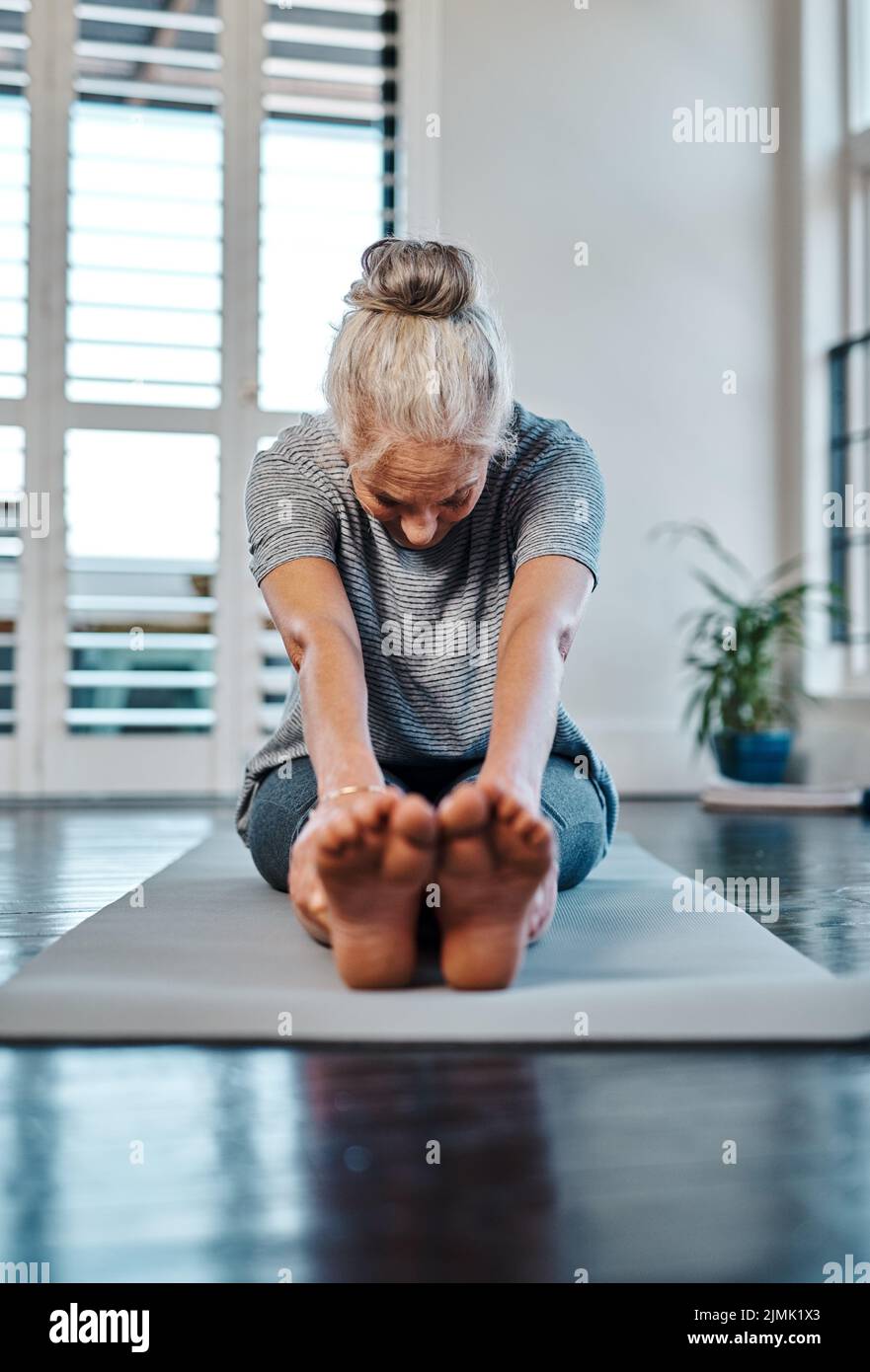 Just a little longer. a relaxed mature woman practicing yoga inside of a studio during the day. Stock Photo
