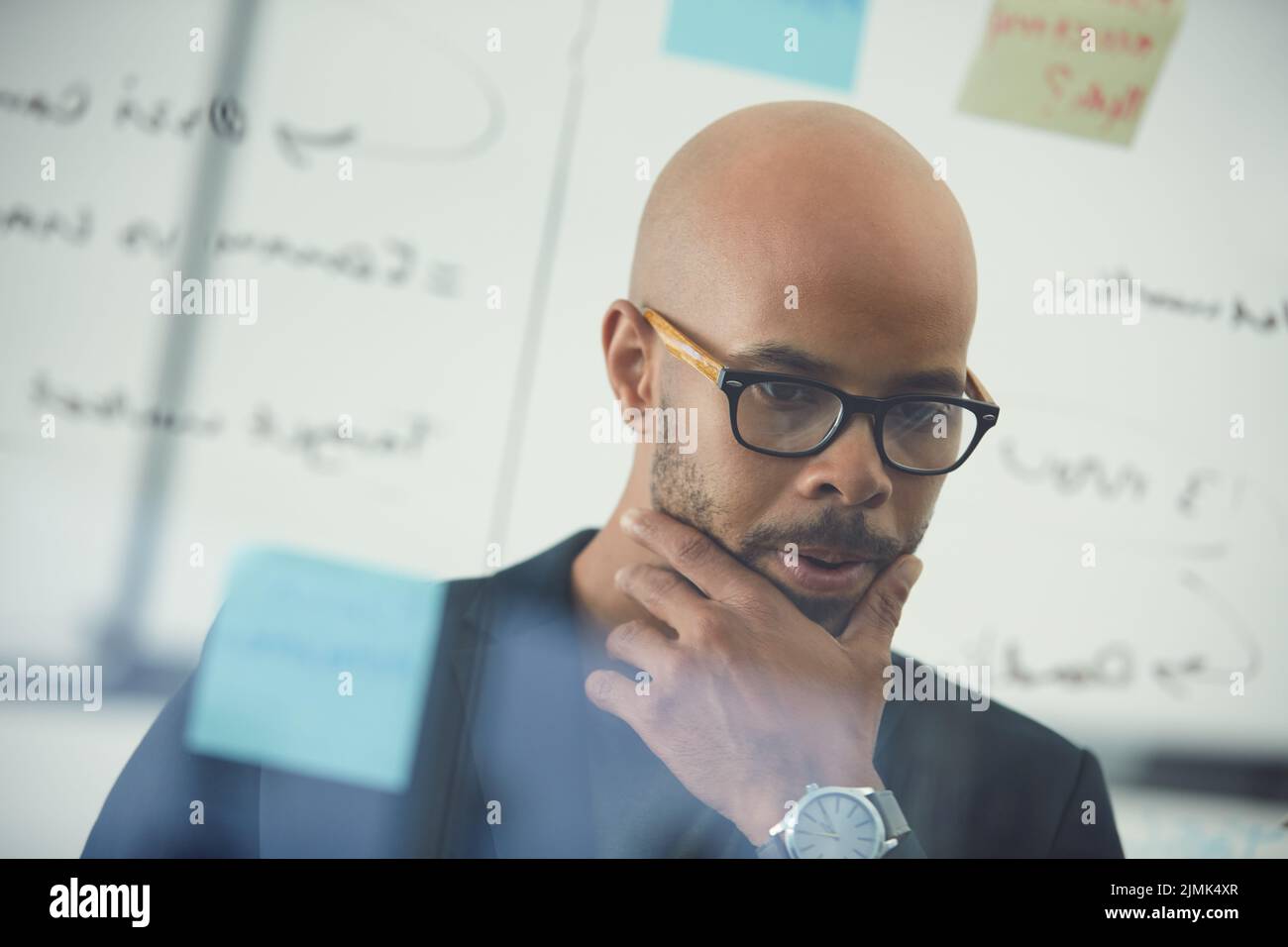 Its taking me longer than expected to solve this. a young businessman brainstorming with notes on a glass wall in an office. Stock Photo