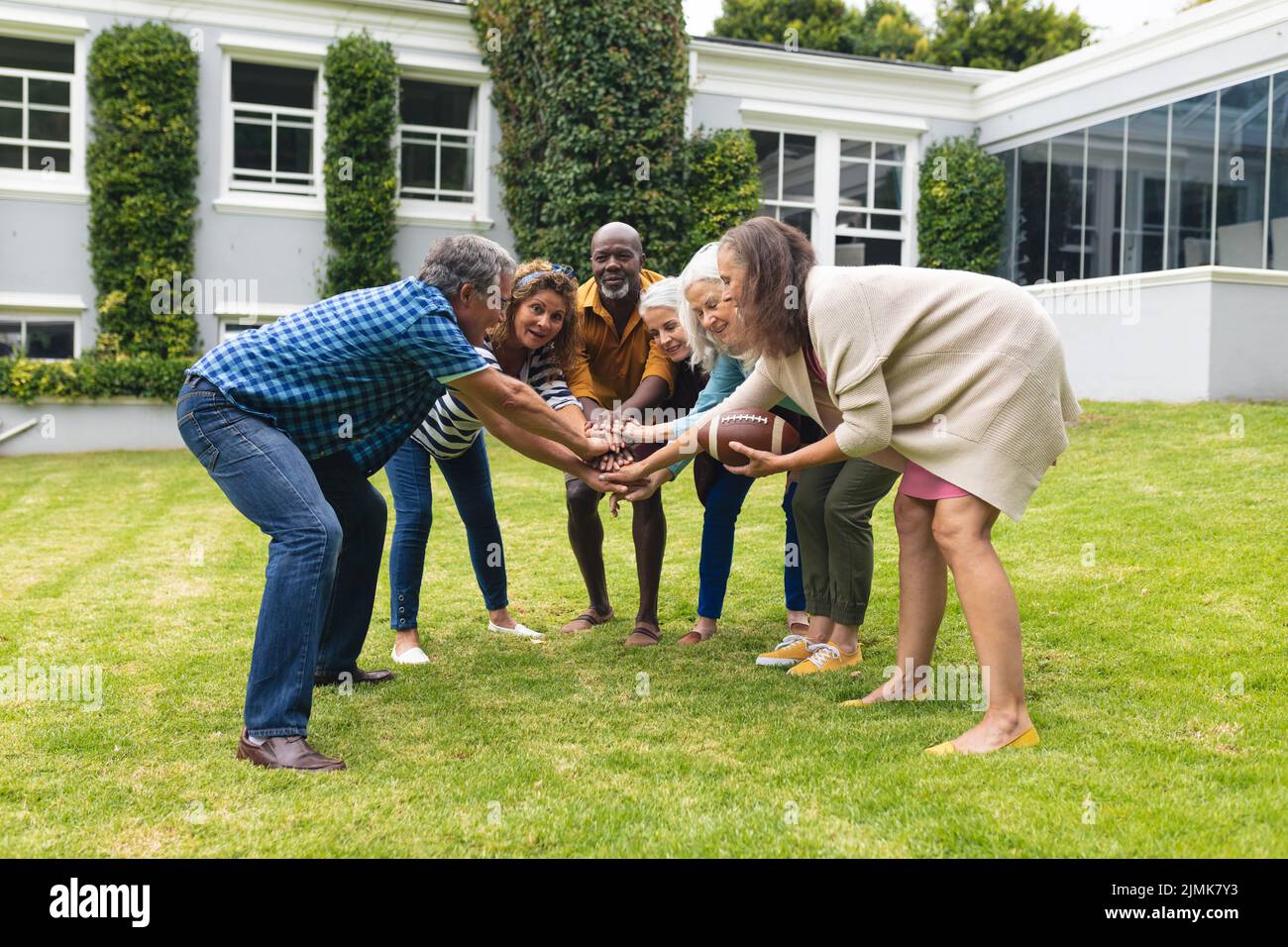 Multiracial senior male and female friends stacking hands while playing ...