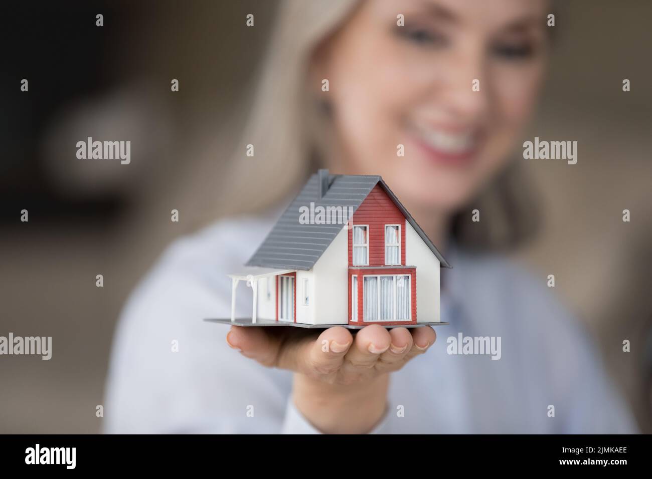 Happy realtor woman holding tiny house model on hand Stock Photo
