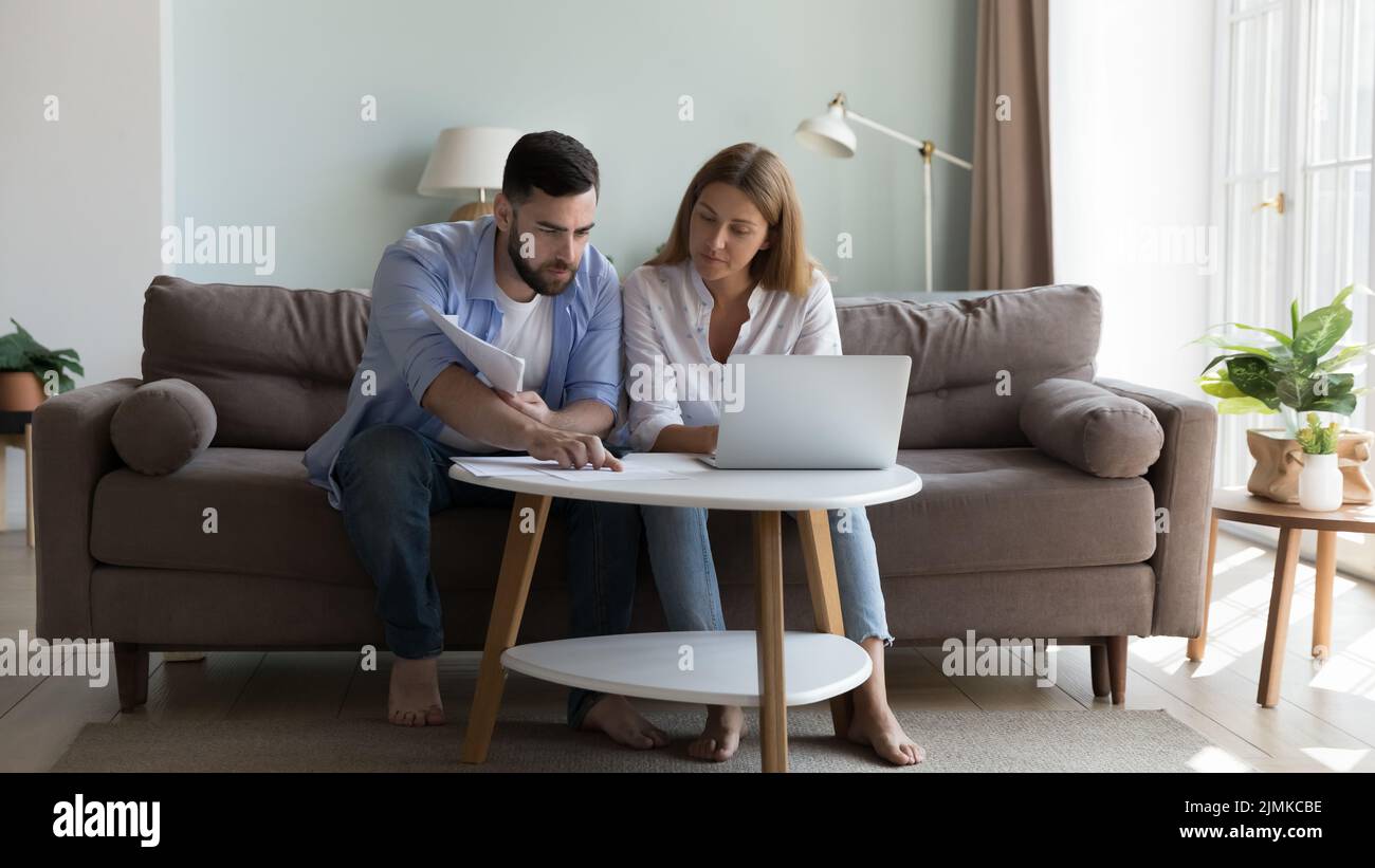 Serious millennial couple sit on sofa sorting out papers Stock Photo