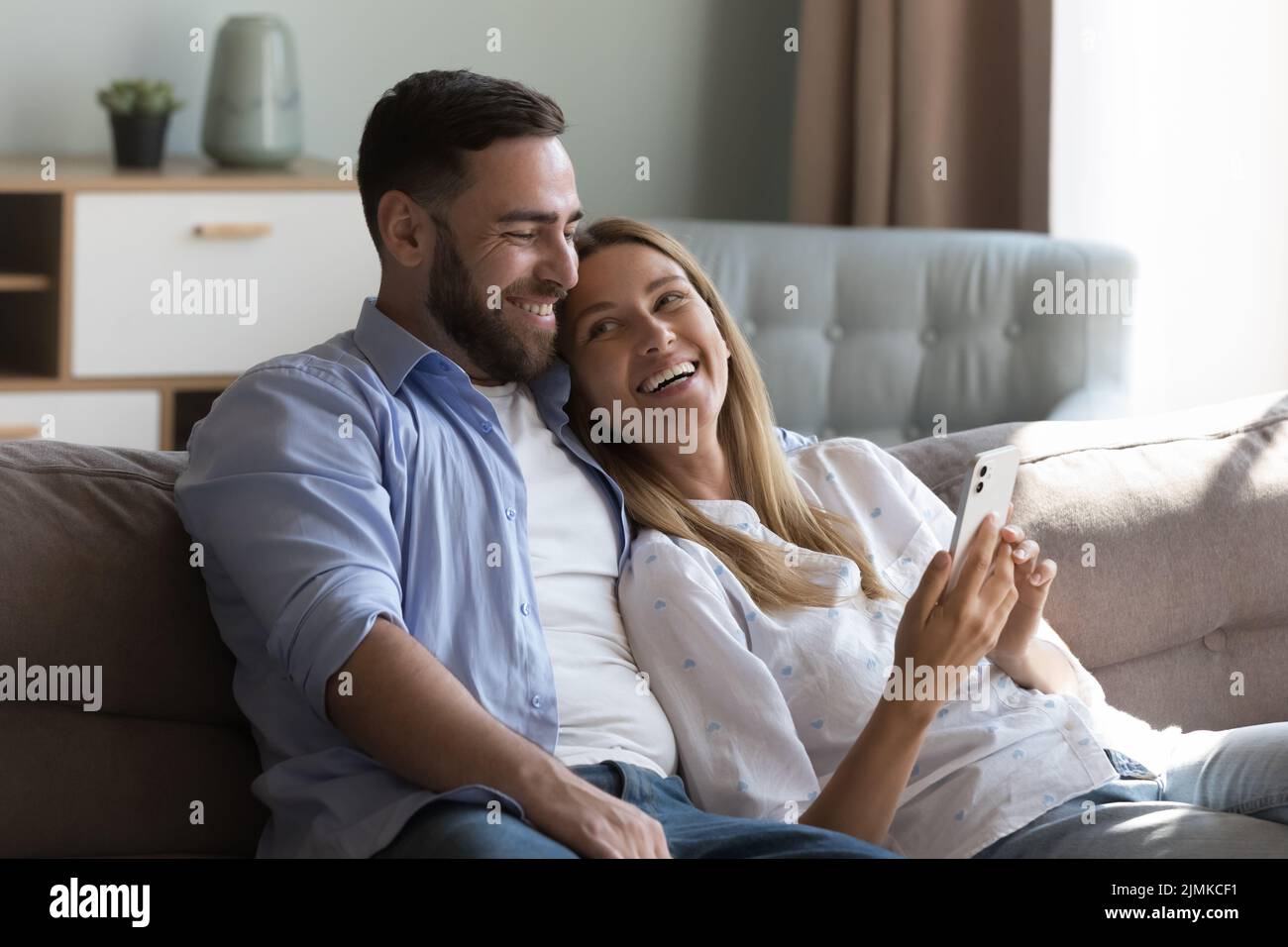 Pretty laughing couple relaxing on sofa using smartphone Stock Photo