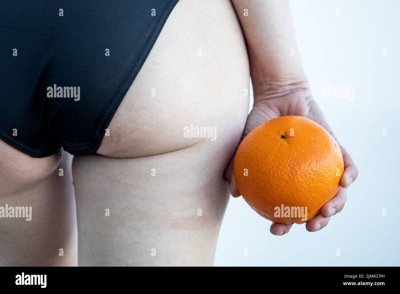 Cellulite or orange skin effect. Woman holding orange by her legs. Stock Photo