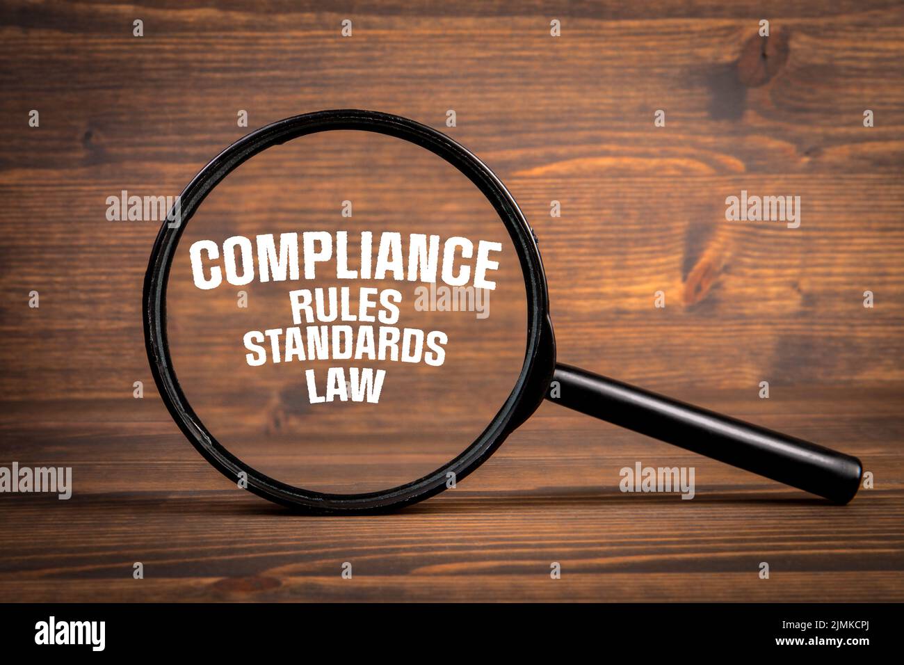 Compliance concept. Magnifying glass on a dark textured wooden background. Stock Photo