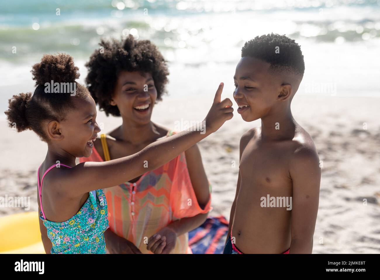 Cheerful african american girl applying suntan lotion on brother's nose