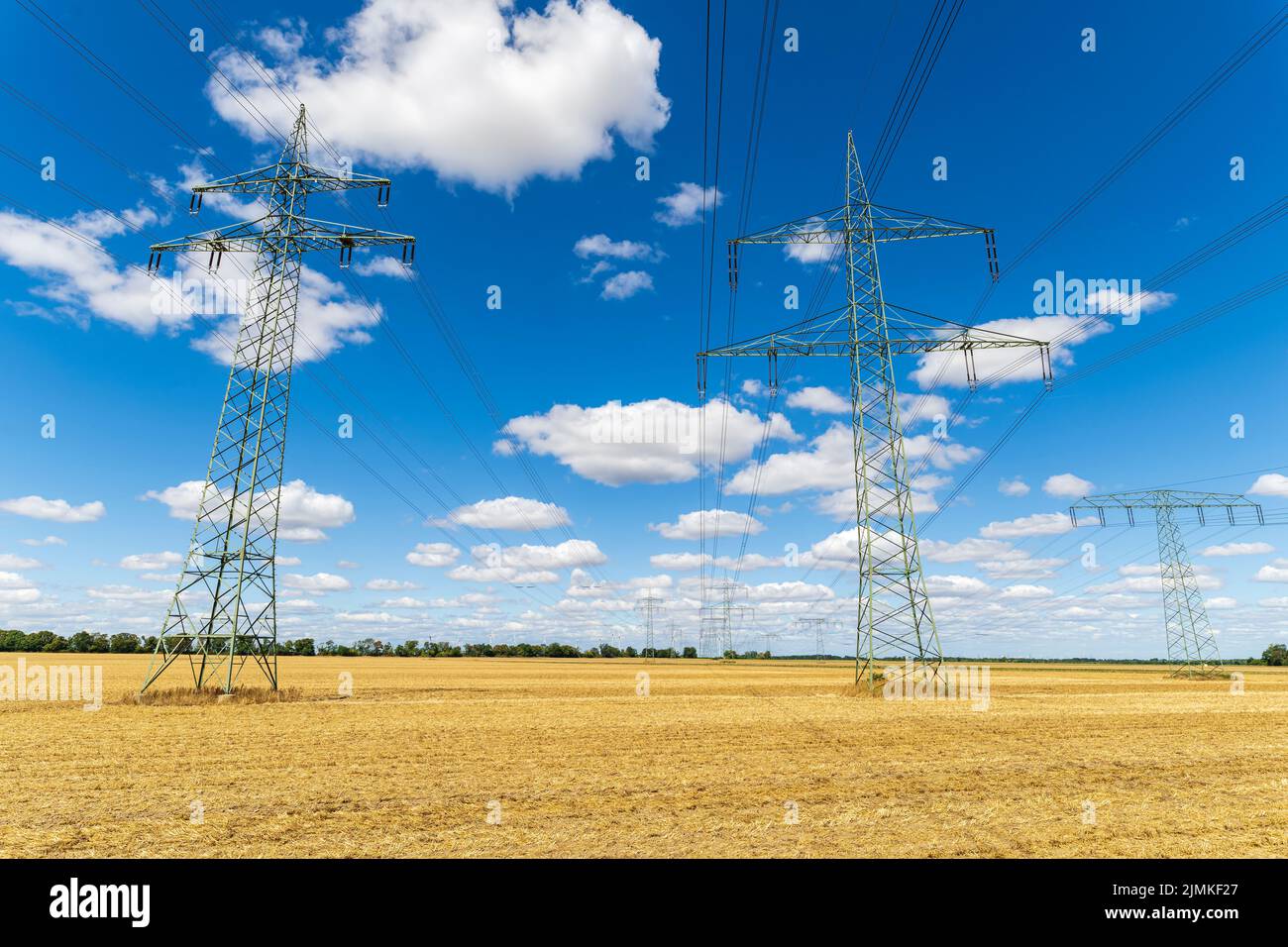 Power pylons of overhead power line under blue sky with clouds Stock Photo