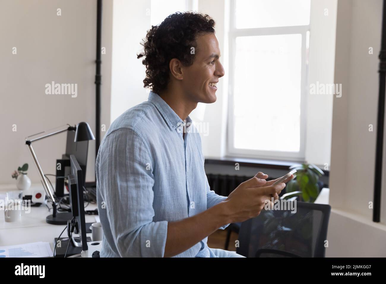 Smiling successful Hispanic businessman using smartphone at workplace Stock Photo