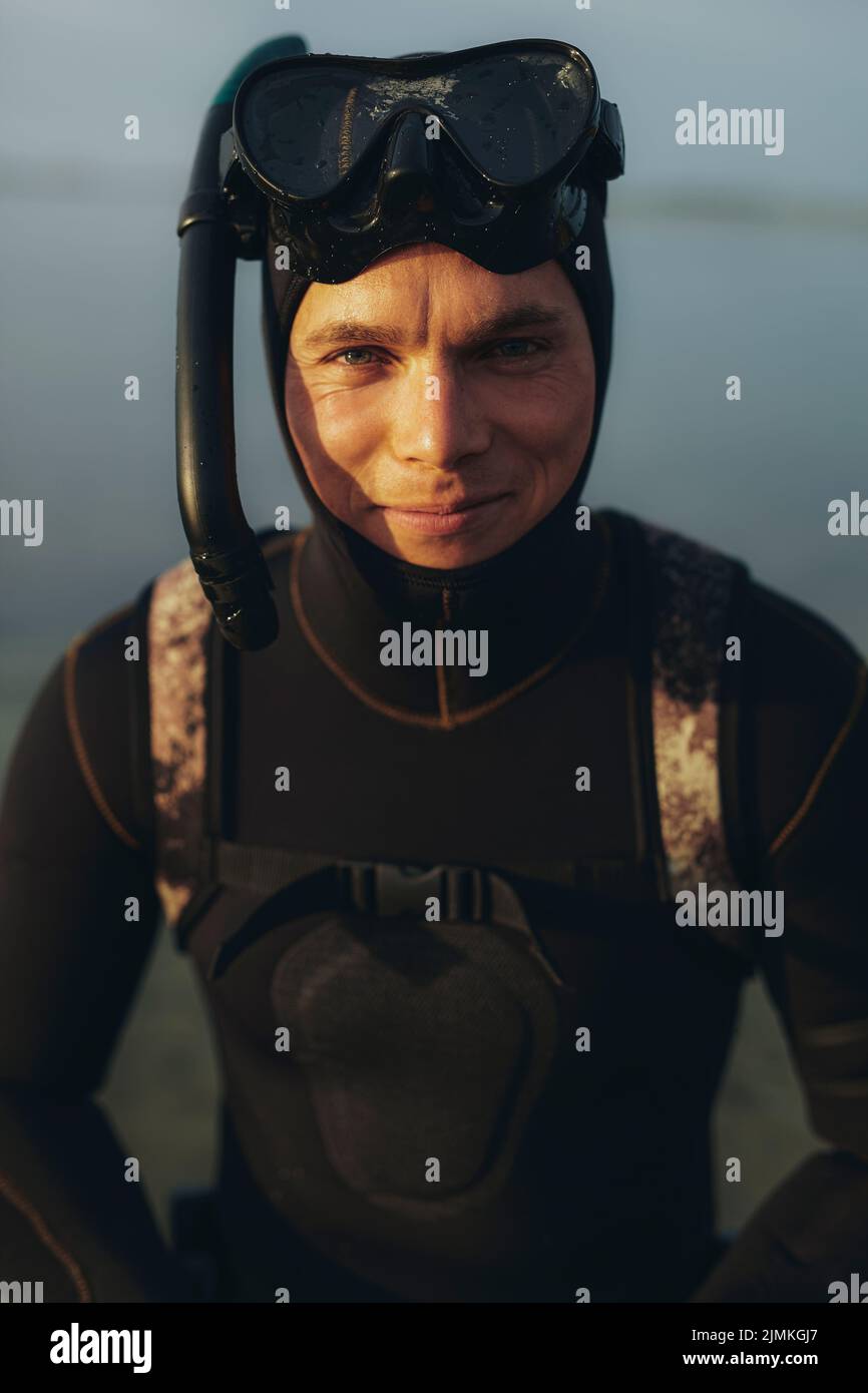 Portrait of an adventurous young man looking at the camera while wearing a scuba gear and a wetsuit. Male diver going scuba diving by the sea. Stock Photo