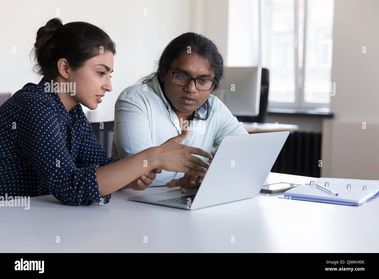 Indian workers sit at desk near laptop discuss new software Stock Photo