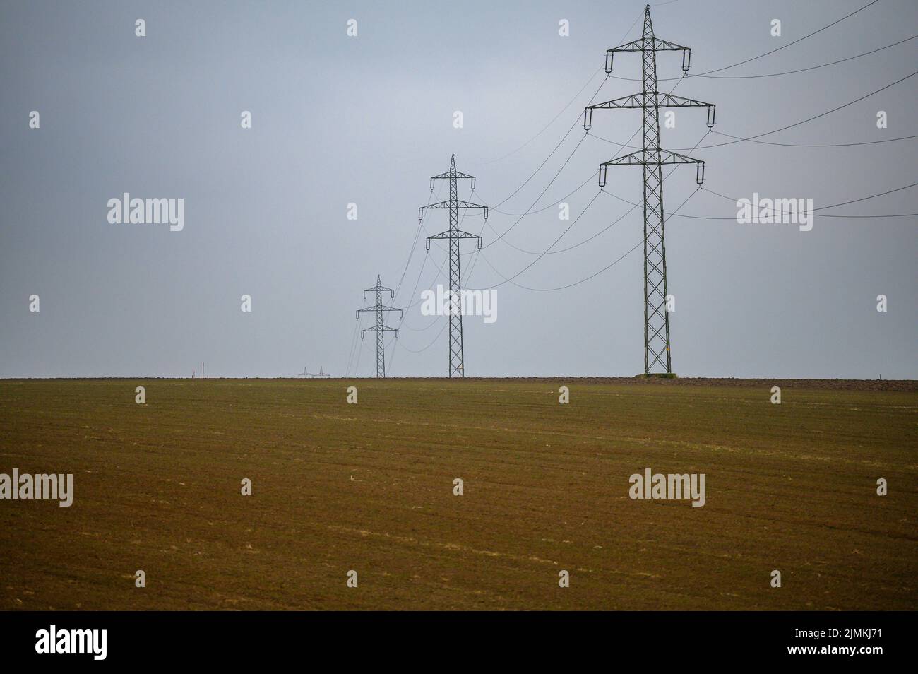 A high-voltage line runs over a bald field. The gray clouds of fog reinforce the wintry impression of the landscape. Stock Photo