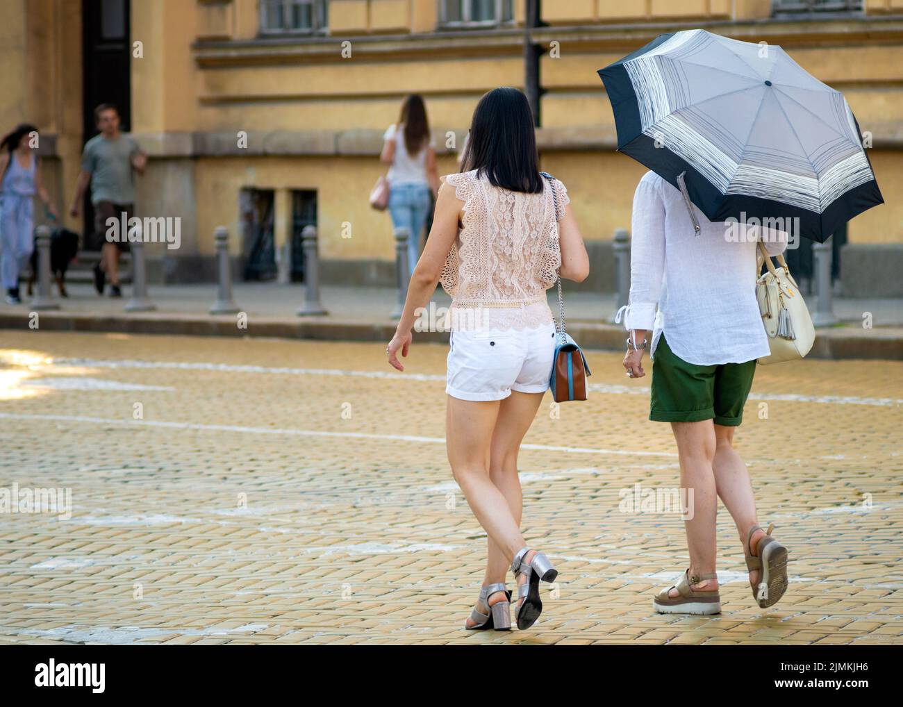 Asian female tourists with umbrella walking on yellow cobblestones paved Tsar Osvoboditel street in downtown Sofia, Bulgaria, Eastern Europe, Balkans, Stock Photo
