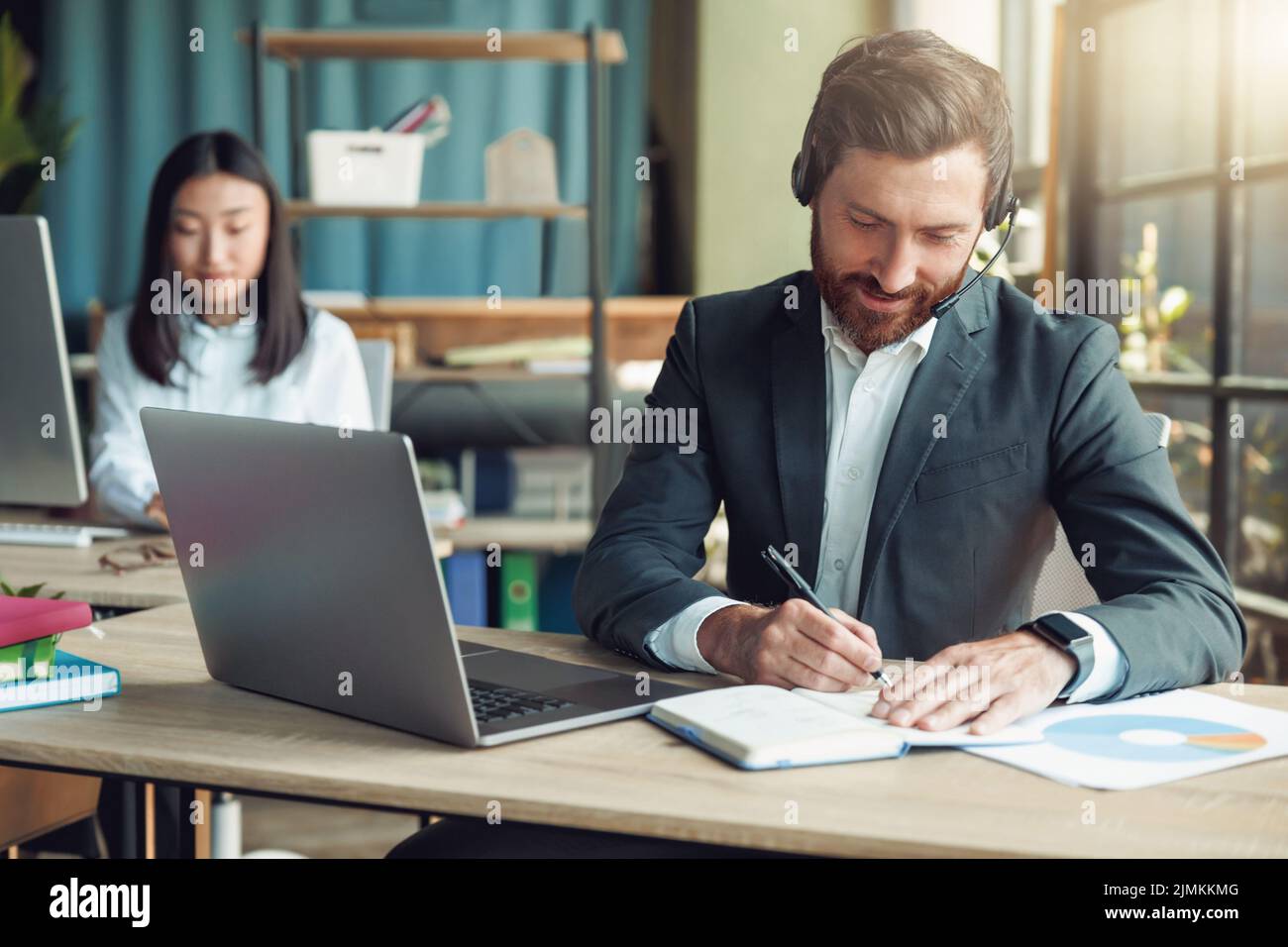Male operator using headset and computer while talking with customers online on colleague background Stock Photo