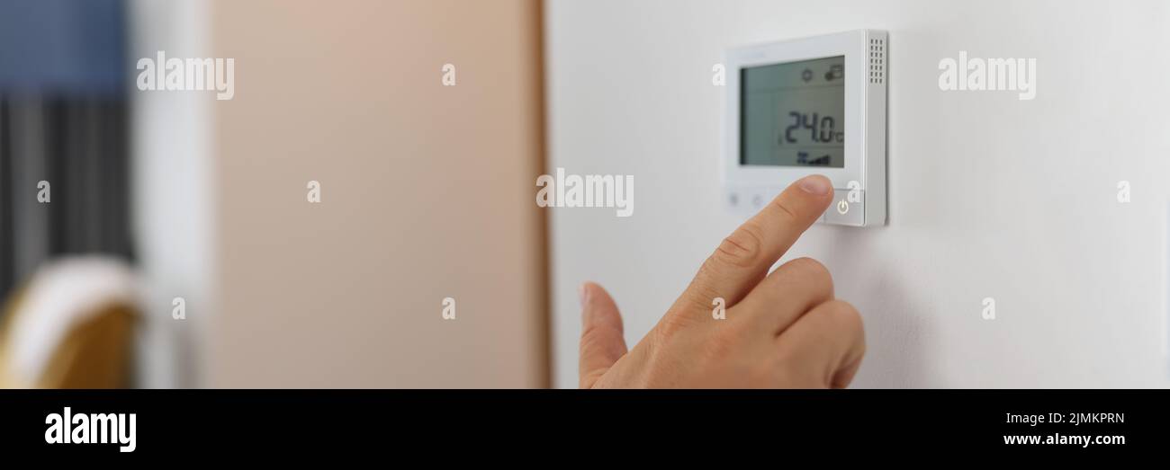 Hand sets a programmable thermostat for heating and cooling Stock Photo