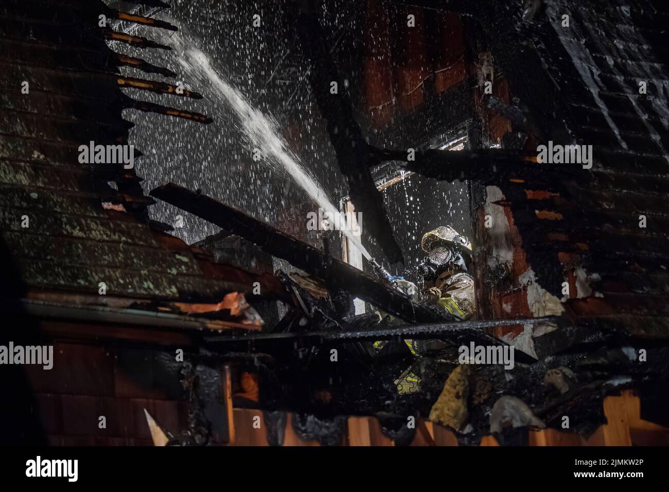 A firefighter hoses down the inside of a burned-out bedroom through a window as Amagansett Fire Department firefighters fight a working fire in a gara Stock Photo