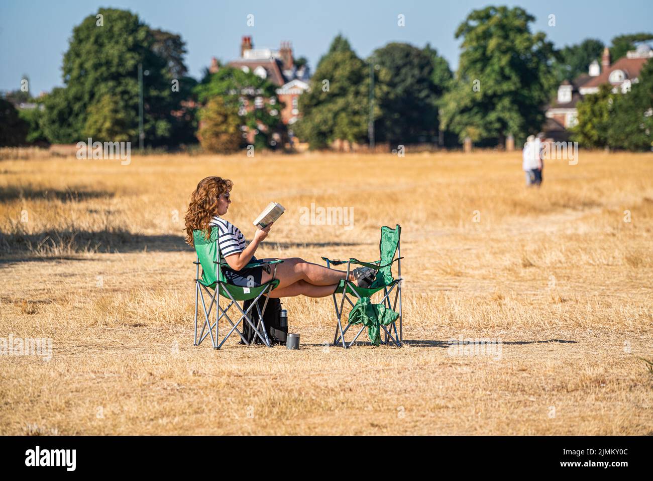 Wimbledon, London, UK. 7 August 2022  A woman sitting with a book on a deckchairs  on a bright morning surrounded by the  parched  grass of Wimbledon Common, south west London  as the hot weather and a lack of rainfall continue to grip much of the south of England and the UK, with temperatures expected to reach  above 30celsius  by next week Credit. amer ghazzal/Alamy Live News Stock Photo