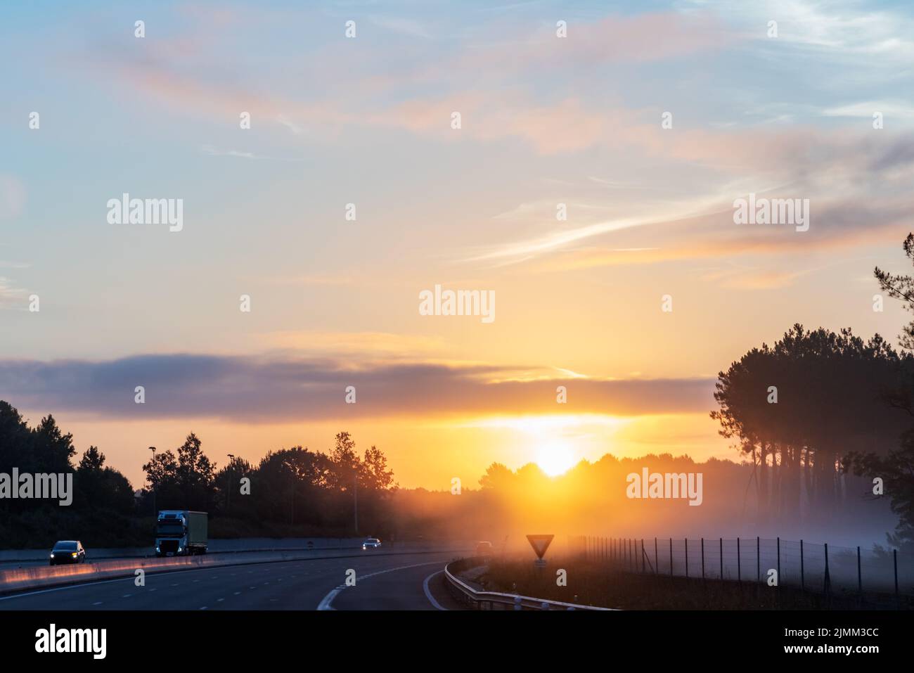 Landscape of a highway at dawn with the sun beginning to rise and the mist between the trees. Stock Photo
