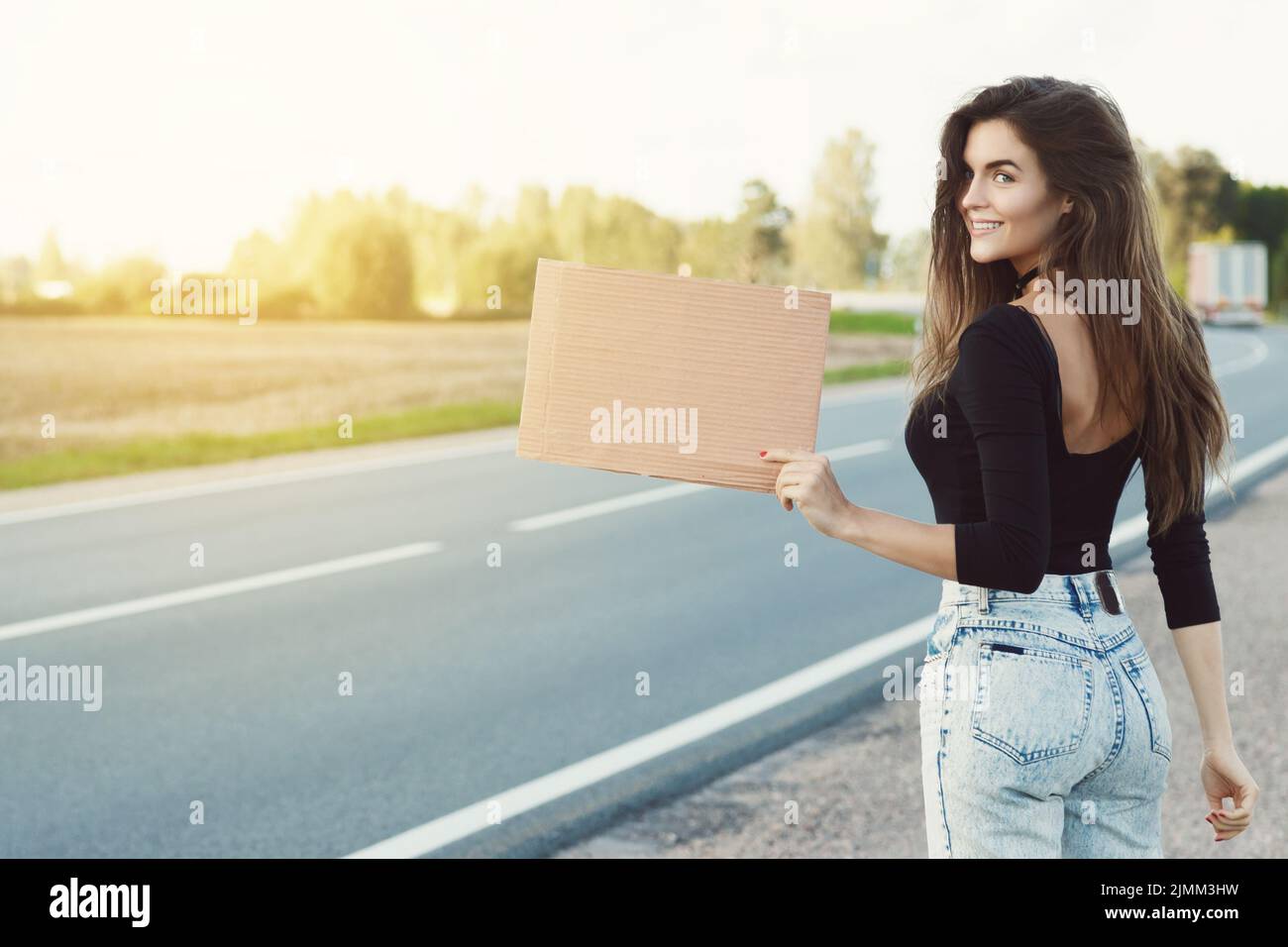 Hitchhiker on the road is holding a blank cardboard sign Stock Photo