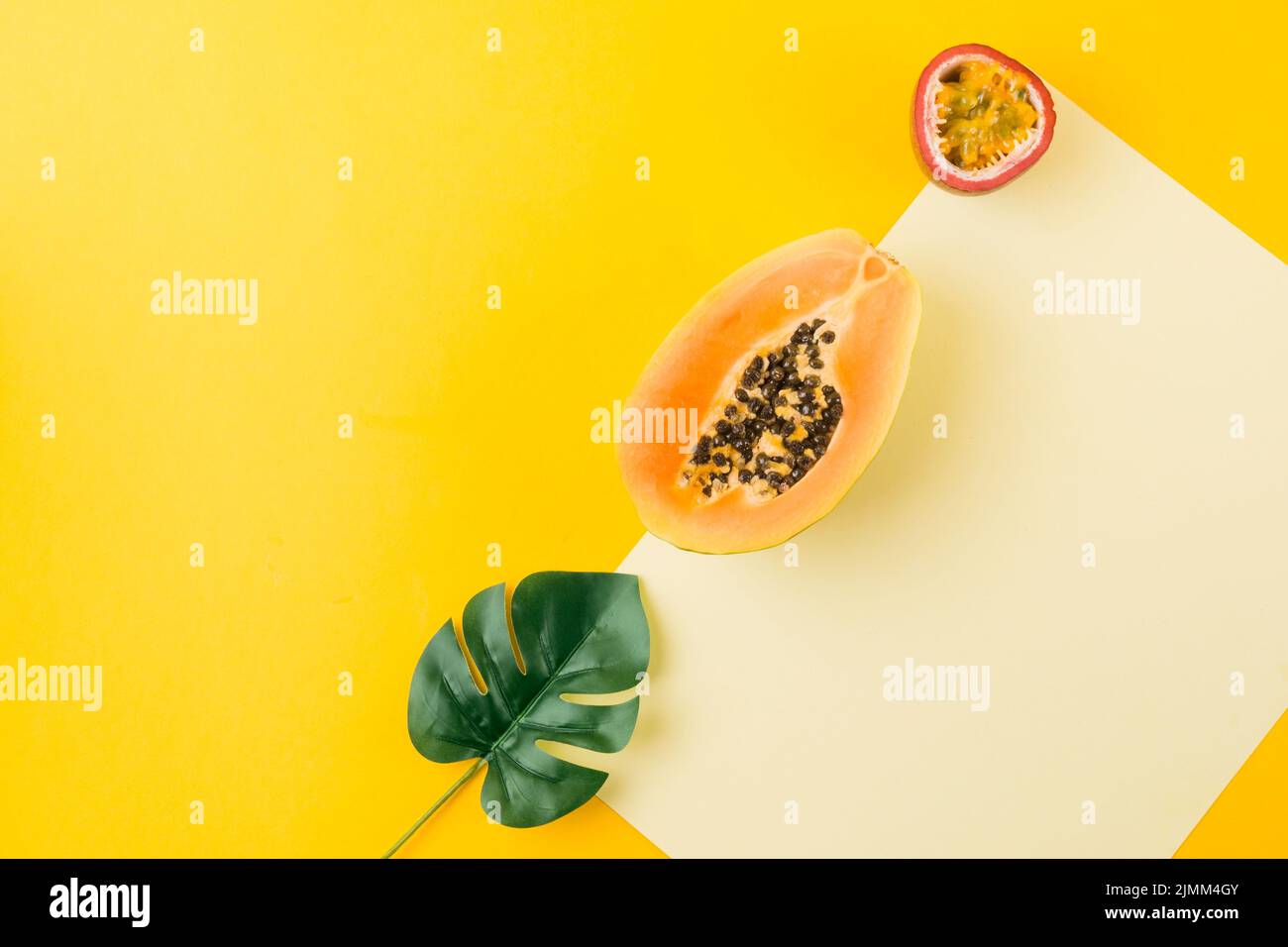 Overhead view artificial leaf papaya passion fruit blank paper against yellow backdrop Stock Photo