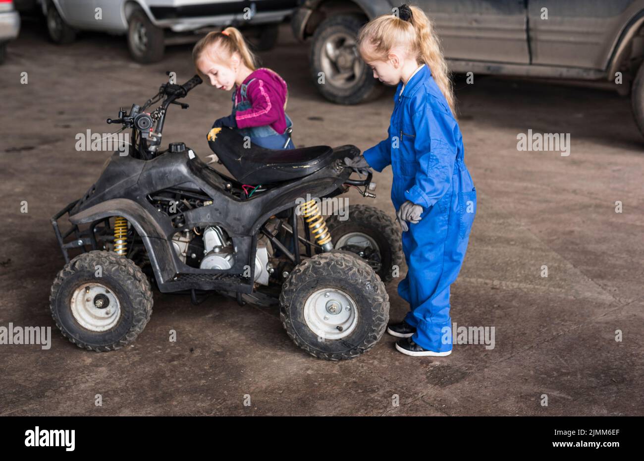Two little girls overalls inspecting quad bike Stock Photo