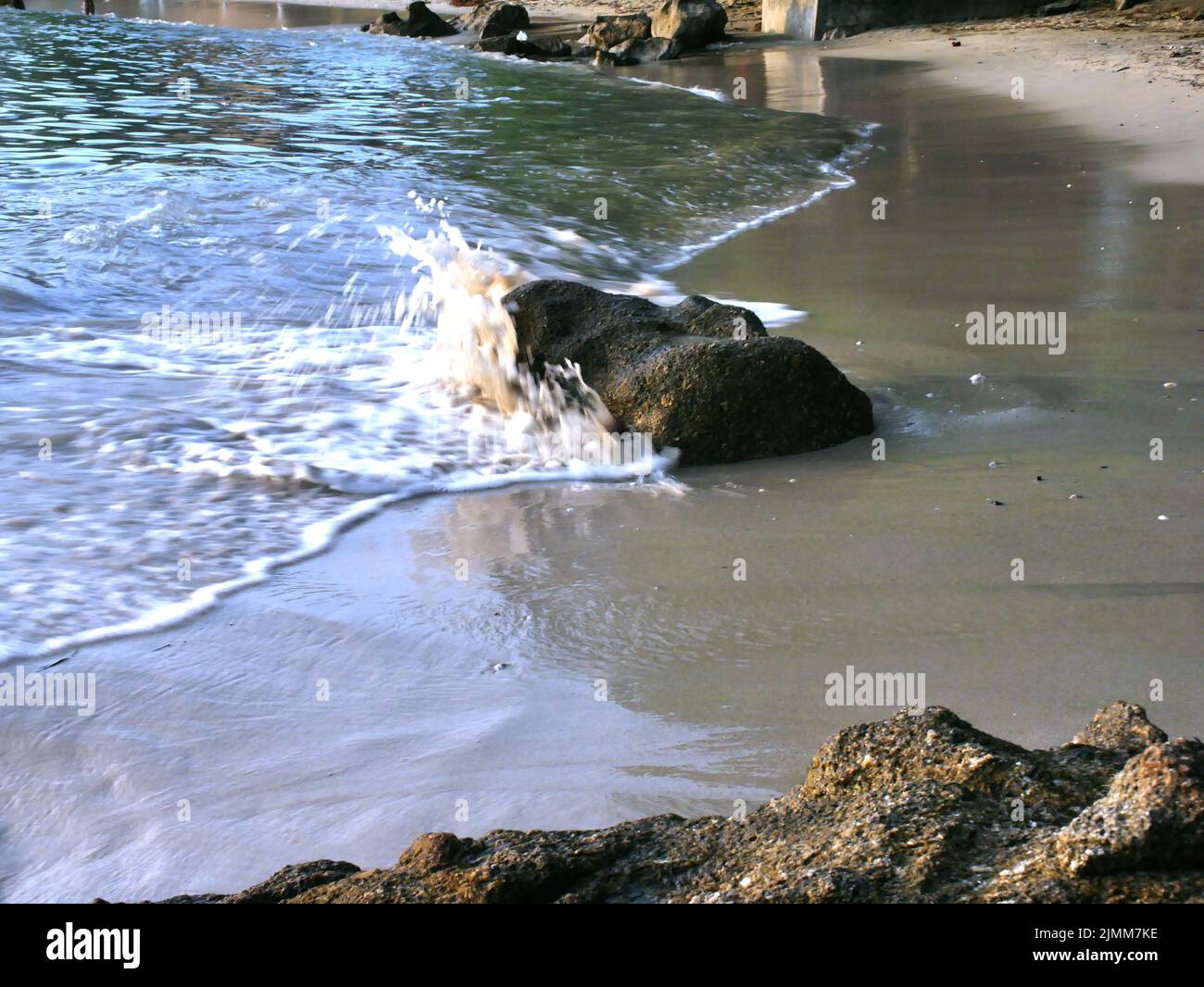A scenic view of sea waves crashing against a rock on a sandy beach ...