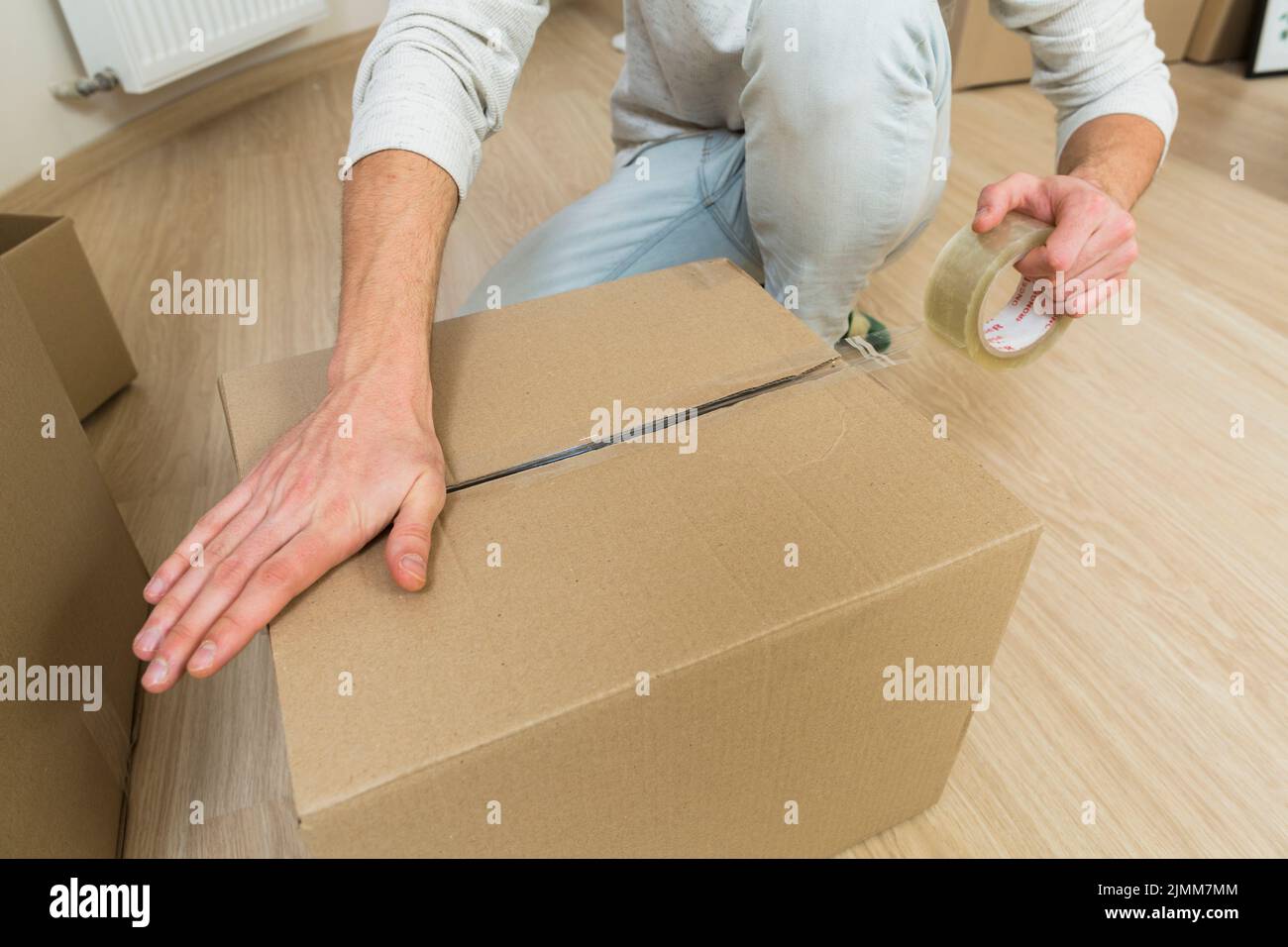 Close up male sealing cardboard box with adhesive tape Stock Photo