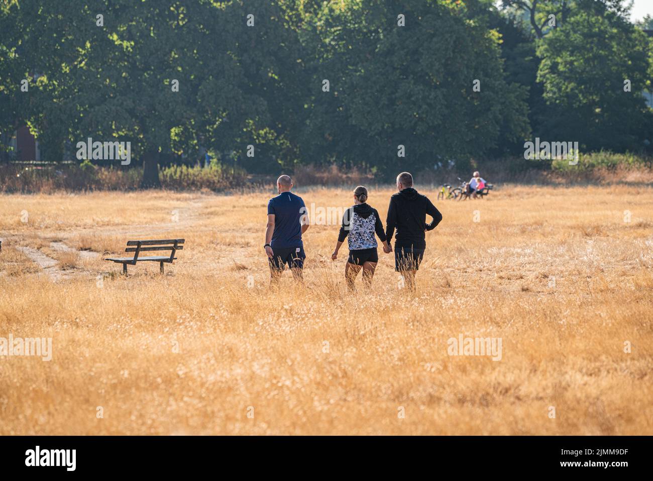 Wimbledon, London, UK. 7 August 2022  People walking on the parched sunburnt  grass  on a bright morning on Wimbledon Common, south west London  as the hot weather and a lack of rainfall continue to grip much of the south of England and the UK, with temperatures expected to reach  above 30celsius  by next weekCredit. amer ghazzal/Alamy Live News Stock Photo