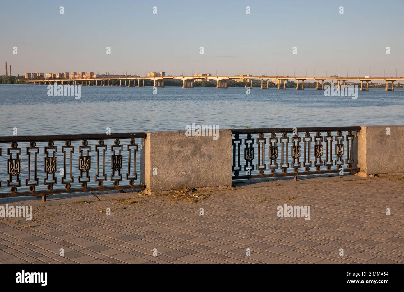 View over Central Bridge over Dnieper river in Dnipro, Ukraine. Embankment fence with Ukrainian Coat of arms. Stock Photo