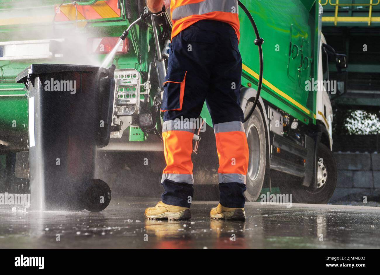 Caucasian Garbage Truck Operator Pressure Washing Black Trash Can After