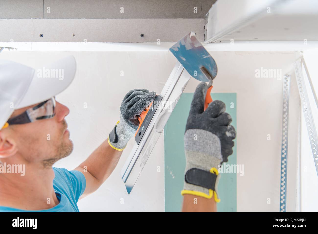 Closeup of the Male Worker Applying Gypsum Wall Putty with Scrapper Putty Knife Tool. House Renovation Work Theme. Stock Photo