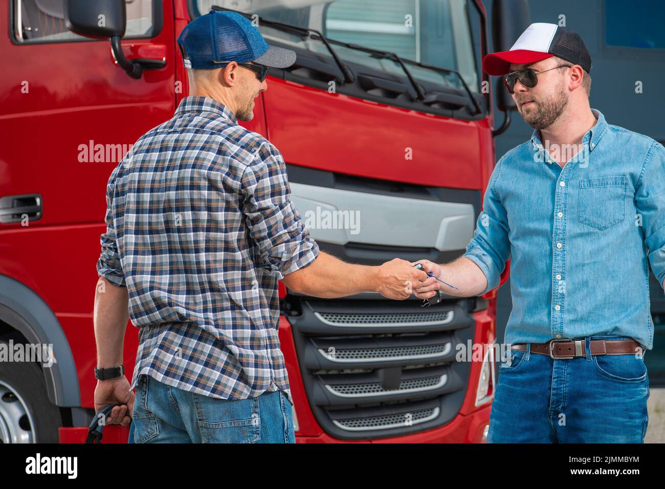 Closeup of Two Caucasian Truck Drivers Swapping the Keys in Front of Red Lorry Cabin Changing Their Shifts For Safe and Secure Delivery of Heavy Duty Stock Photo
