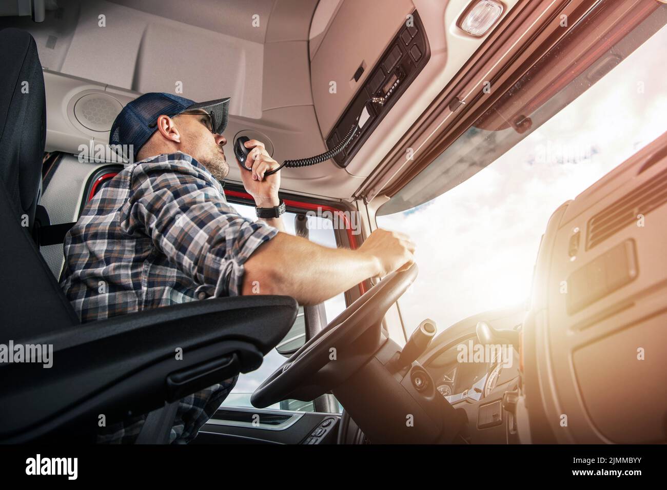 Caucasian Middle Aged Truck Driver Talking Via Citizen Band Radio During Completing a Delivery of His Cargo. Side View Photo Inside the Lorry Cabin. T Stock Photo