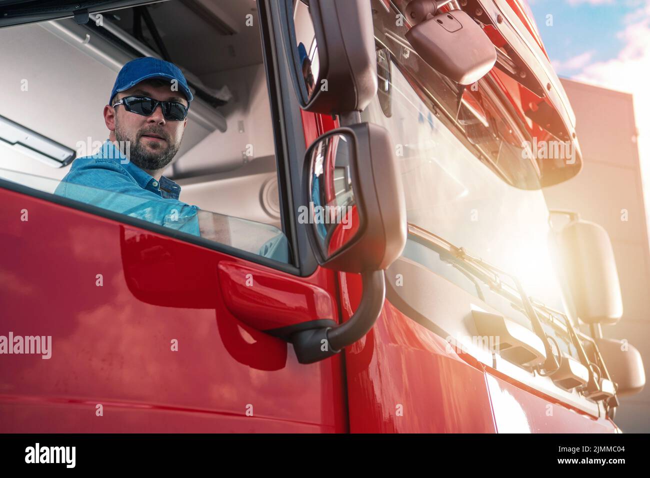 Caucasian Trucker in His 30s Sitting in the Passenger Sear of a Red Semi Truck Looking Out of an Open Window. Resting During a Long Drive. Transportat Stock Photo